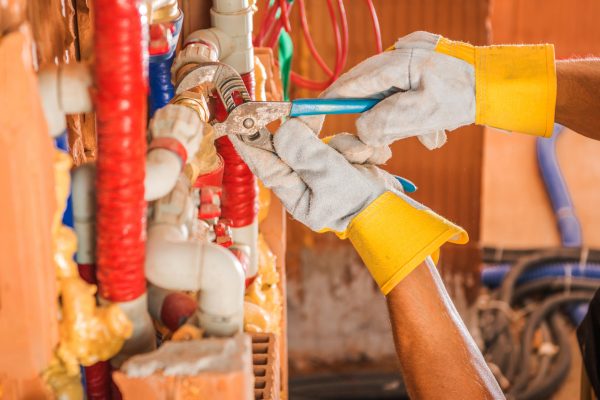 Caucasian Plumber Finishing Whole New Water Supply System Inside Concrete Blocks Build Commercial Building. Close Up on His Hands.