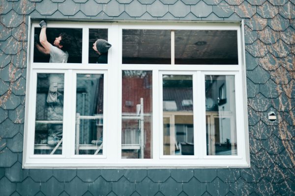 Two young handsome Caucasian men manually repair a window with plastic frames from the outside on a spring day, side view, medium plan. Concept for repair and installation of windows.